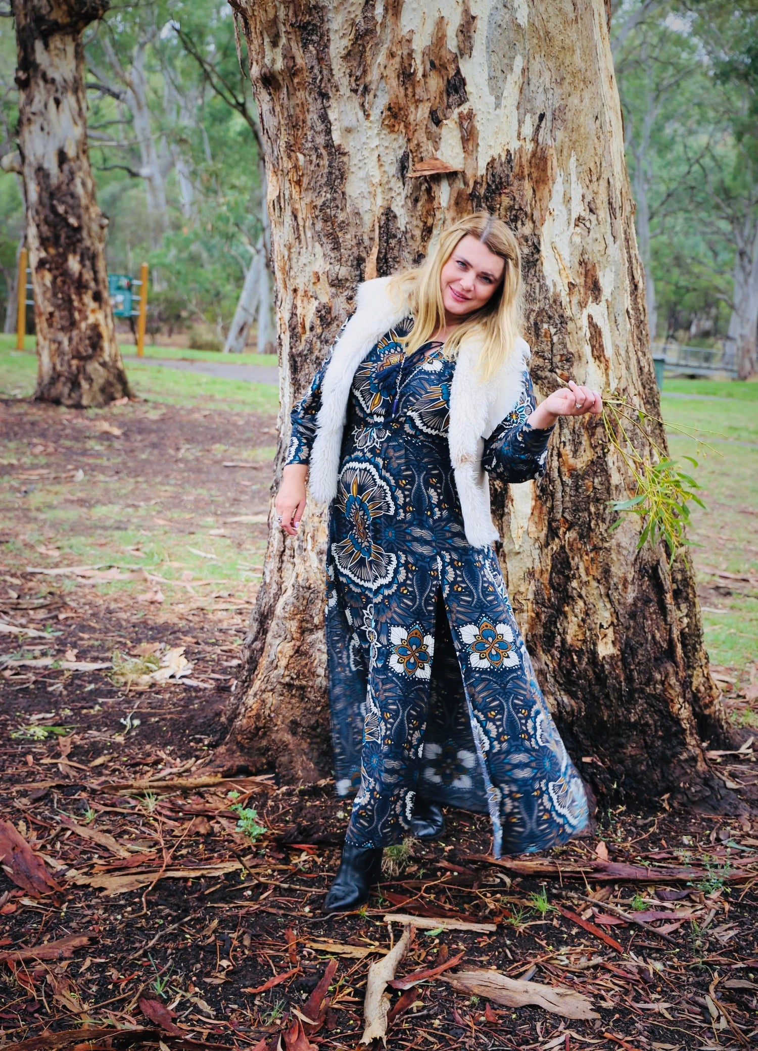 Tanja Boldt standing under a tree, smiling in a beautiful long floral dress, representing the face of Jaroma Tea's holistic wellness.