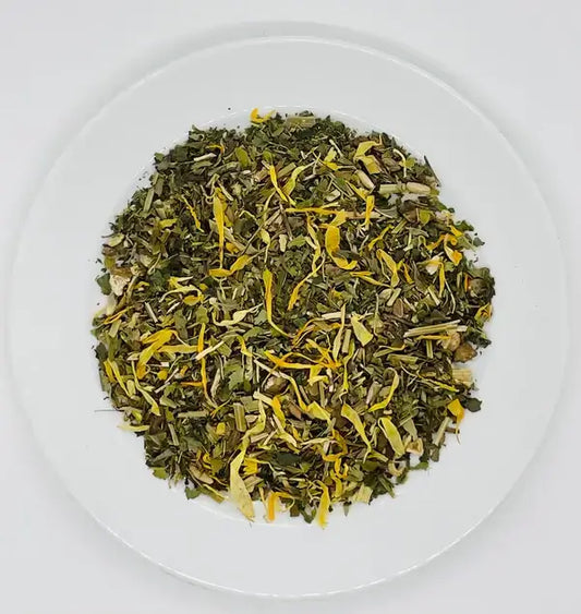 A close-up shot of loose-leaf Jaroma Goddess Bliss Tea, showcasing a blend of green tea leaves mixed with vibrant yellow calendula petals and other aromatic herbs. The tea blend exudes a calming, vibrant look on a white plate.