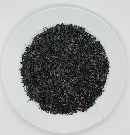 A close-up shot of premium black tea leaves from Jaroma, showcasing a blend of dark, rich leaves with hints of yellow and green. The tea leaves are spread evenly in a circular pattern, offering a visual appeal that invites a flavorful and robust brew.