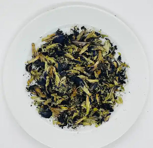 Loose leaf organic butterfly pea flowers, showcasing the blue and green hues of the petals on a white plate, ready for infusion in Jaroma Blue Magic Tea.
