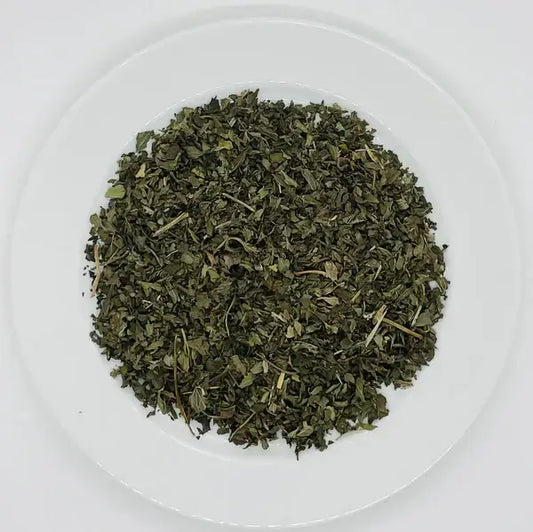 A close-up of loose-leaf Jaroma Peppermint Tea, arranged in a circular pattern on a white plate. The vibrant green leaves, finely chopped, are the organic peppermint leaves, ready for brewing to create a refreshing and soothing herbal tea.
