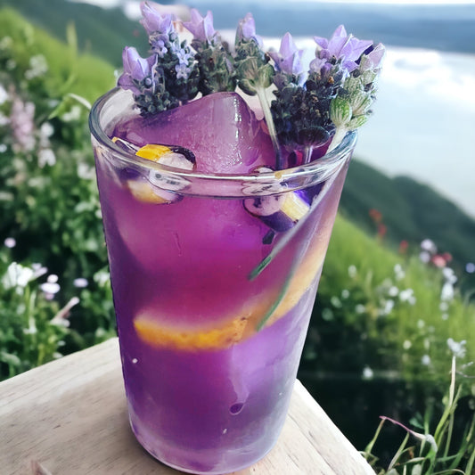 A vibrant glass of butterfly pea flower tea with a striking purple color, adorned with fresh lavender sprigs and a twist of citrus, served on a rustic wooden surface with a natural, floral backdrop.