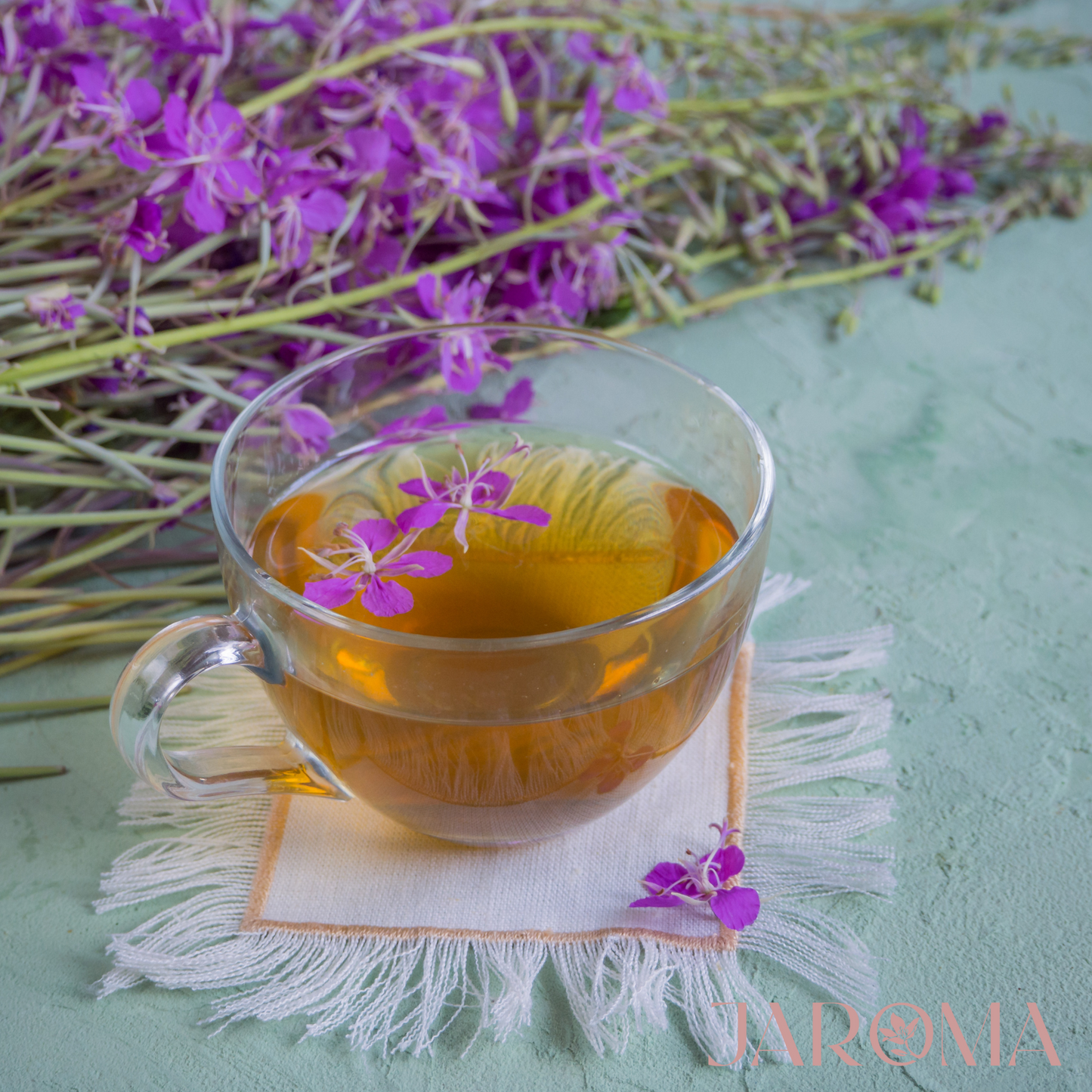 Clear glass cup of tea with a flower on a light green surface with purple flowers in the background
