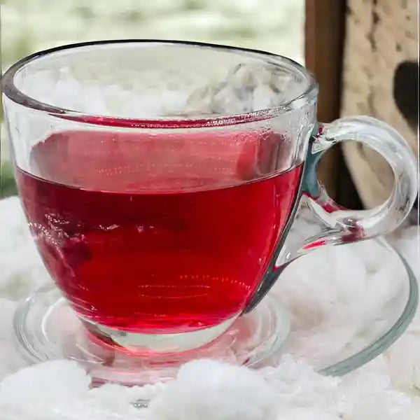 A hot cup of Cherry Berry Delight tea, showcasing the rich, vibrant red colour of the infusion, with the cup resting on a saucer surrounded by soft, fluffy white blanket. 